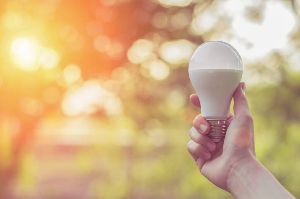 hand holding up an LED lightbulb with sun in background to reduce carbon footprint
