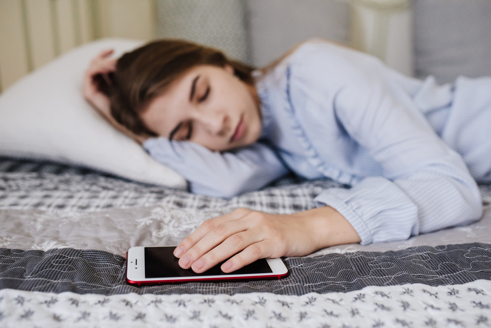 woman in bed sleeping with her hand on her smartphone