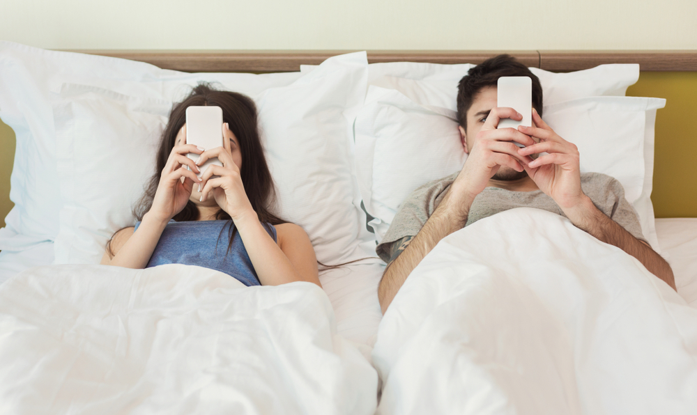 couple laying in bed on their phones "phubbing" - cell phones and relationship problems