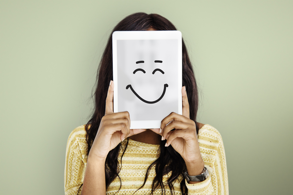 woman holding up a tablet with a happy face drawn on it to show feelings and emotions