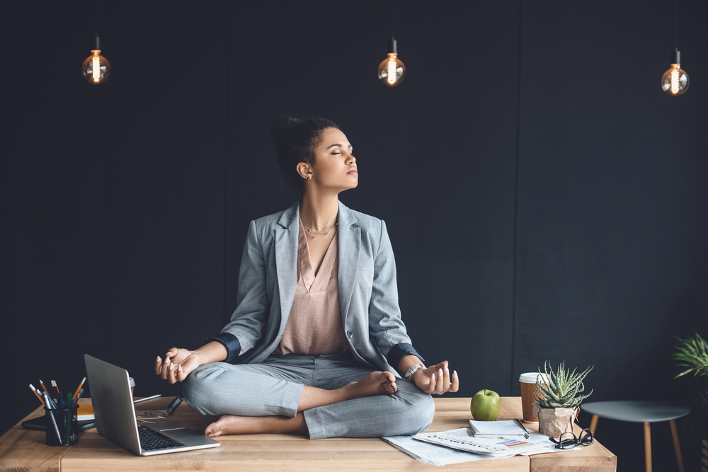 woman practicing meditation in the workplace on her desk in a tranquil black office space