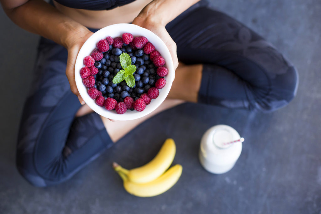a photo of a person holding up a bowl full of blueberries and raspberries in focus while there's a bottle of milk and a couple of bananas laid out on the floor, amid the discussion about the benefit of looking to a nutritional guru for nutritional expert advice