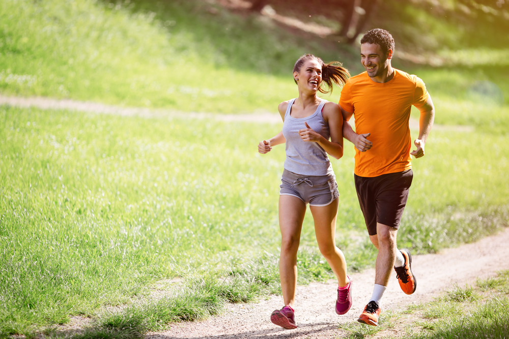 photo of a man and woman running together in a park and enjoying running benefits along the way