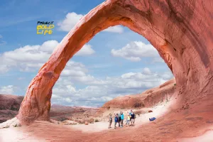 people hiking under a weird rock formation