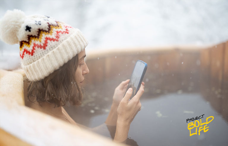 A woman relaxing in an outdoor hot tub while using her smartphone