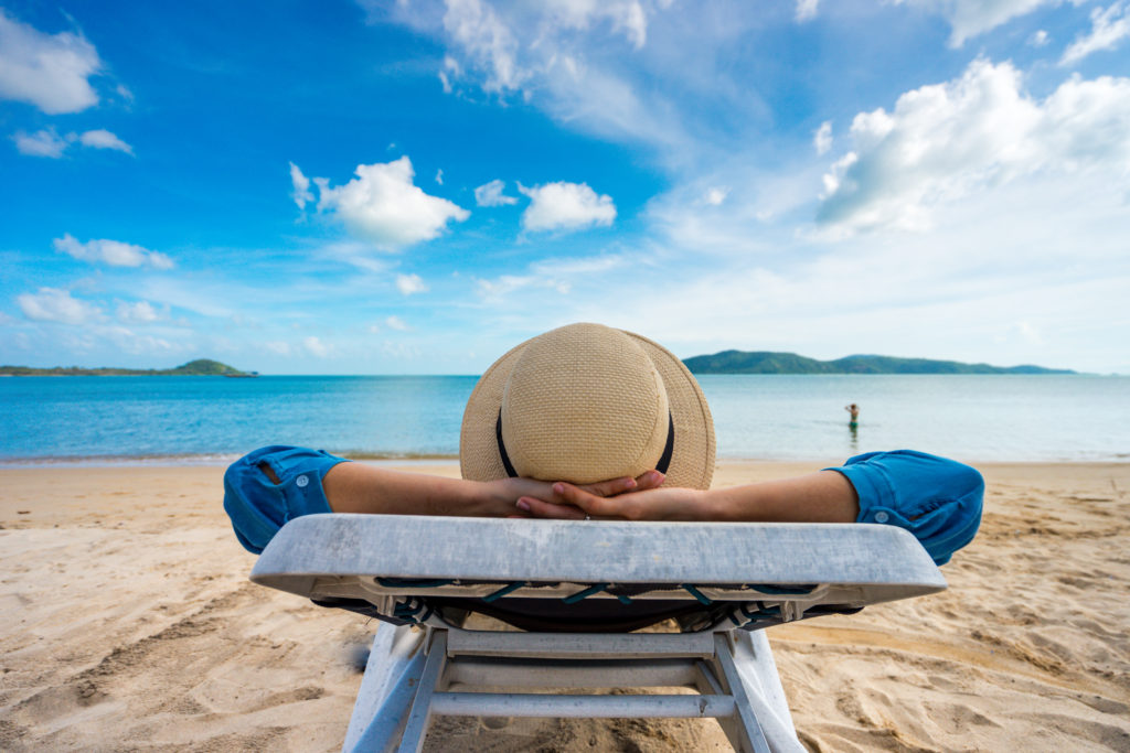 person relaxing on lounge chair on the beach enjoying benefits of a vacation