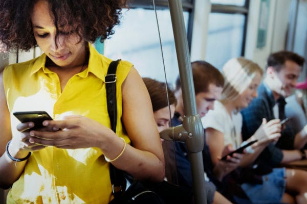 woman standing in bus looking down at her phone