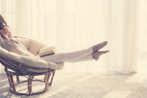 woman practicing self-care while stretching in chair with a book on her lap