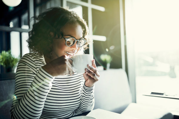 Smiling young woman taking time for herself enjoying fresh coffee in a cafe