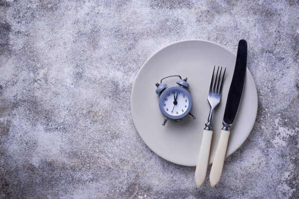 empty plate with clock and utensils illustrating intermittent fasting