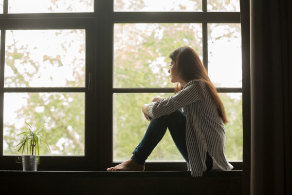 girl battling anxiety, sitting at a window looking out