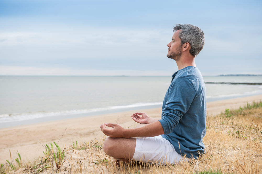 man sitting beachside meditating peacefully