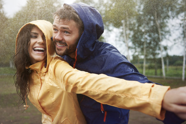 Young couple in rain jackets playing outside in the rain