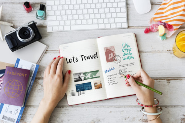 person writing in a travel diary surrounded by items to help her document travels