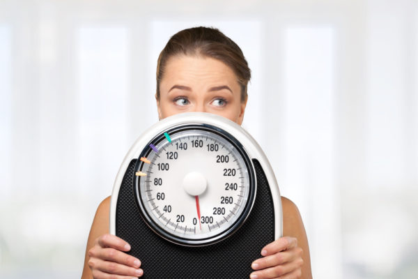 woman holding up a scale in front of her face, thinking about stress and weight loss