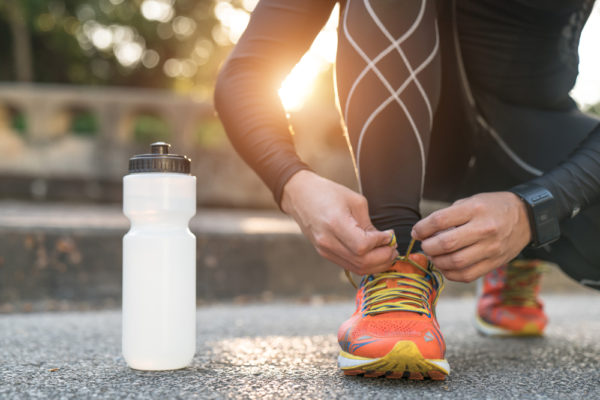 person bending down to tie up shoes next to water bottle – health benefits of walking