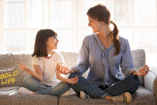 A mom and daughter doing yoga on a couch