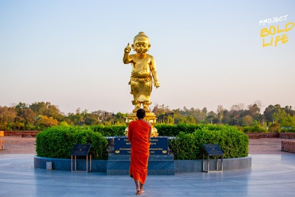 A monk standing in front of a golden Buddha