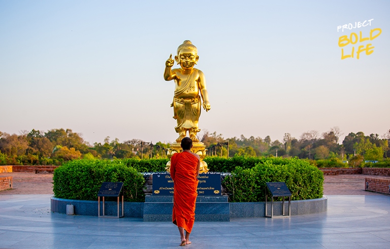 A monk standing in front of a golden Buddha